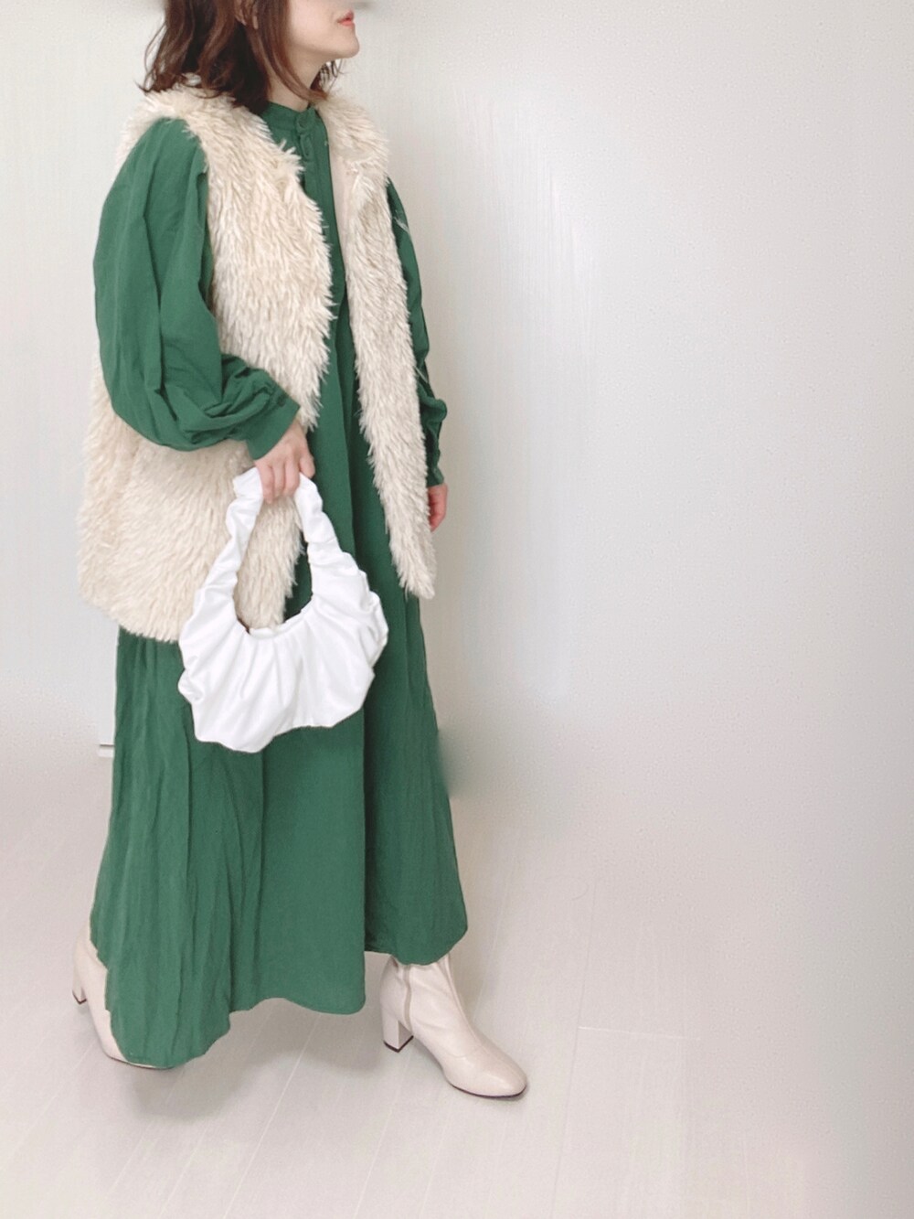 ホワイト系のベスト、グリーン系のワンピース、ベージュ系のブーツを着用したレディースの秋コーディネートの2枚目の写真