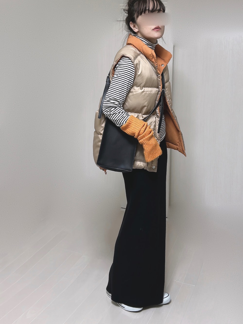 オレンジ系のダウンベスト、ブラック系のショルダーバッグ、ブラック系のスカートを着用したレディースの冬コーディネートの3枚目の写真