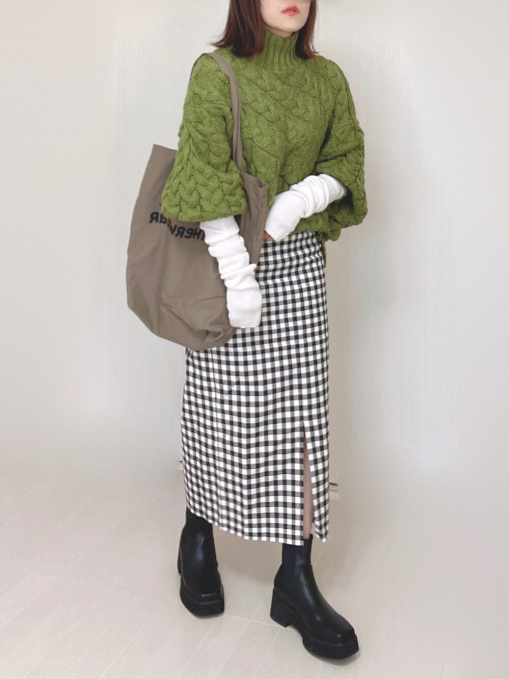 ブラック系のブーツ、グリーン系のニット/セーター、ブラウン系のトートバッグを着用したレディースの冬コーディネートの2枚目の写真