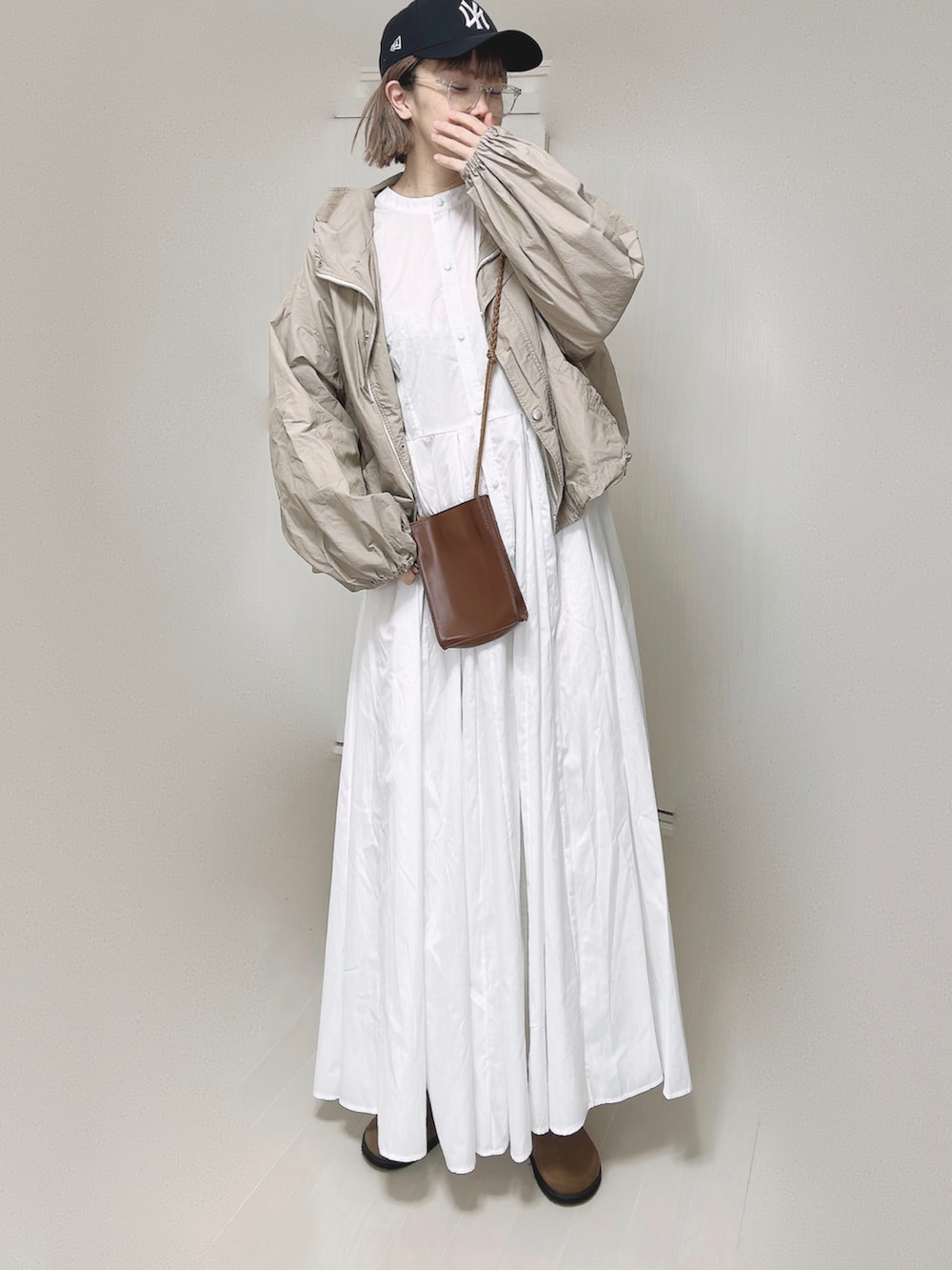 ベージュ系のマウンテンパーカー、ホワイト系のシャツワンピース、ブラウン系のショルダーバッグを着用したレディースの春コーディネートの2枚目の写真