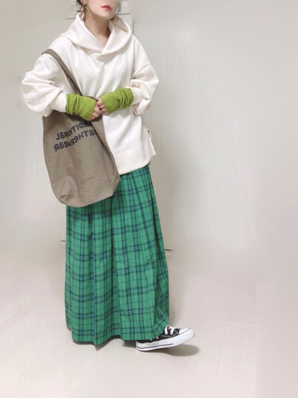 ホワイト系のパーカー、ブラウン系のトートバッグ、グリーン系のスカートを着用したレディースの秋コーディネートの2枚目の写真