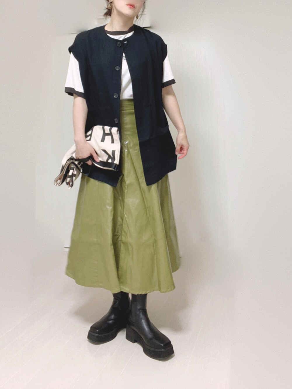 ブラック系のベスト、ホワイト系のトートバッグ、グリーン系のスカートを着用したレディースの秋コーディネートの2枚目の写真