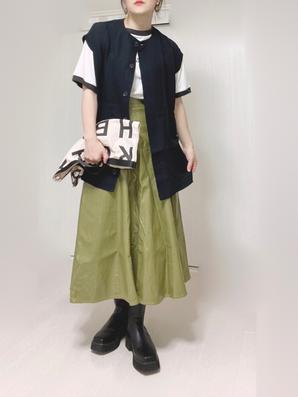 ブラック系のベスト、ホワイト系のトートバッグ、グリーン系のスカートを着用したレディースの秋コーディネートの4枚目の写真