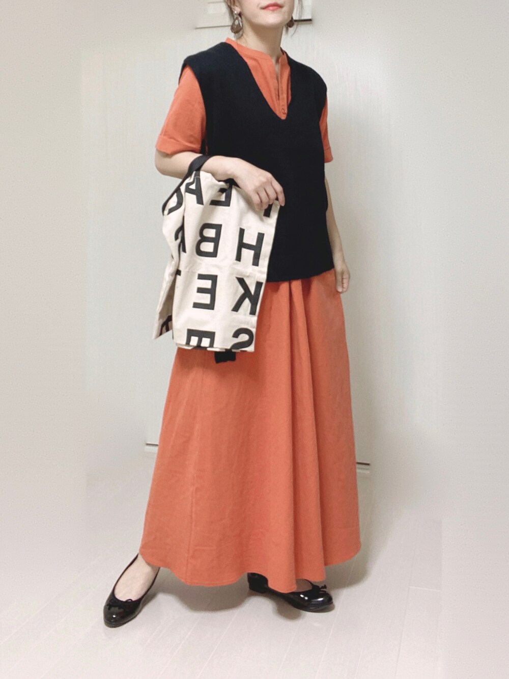 オレンジ系のワンピース、ブラック系のベスト、ホワイト系のトートバッグを着用したレディースの夏コーディネートの2枚目の写真