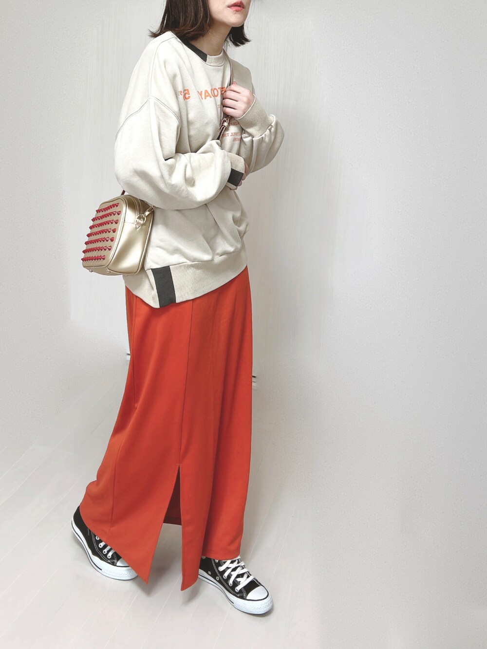 ベージュ系のスウェット、ゴールド系のショルダーバッグ、オレンジ系のスカートを着用したレディースの春コーディネートの2枚目の写真