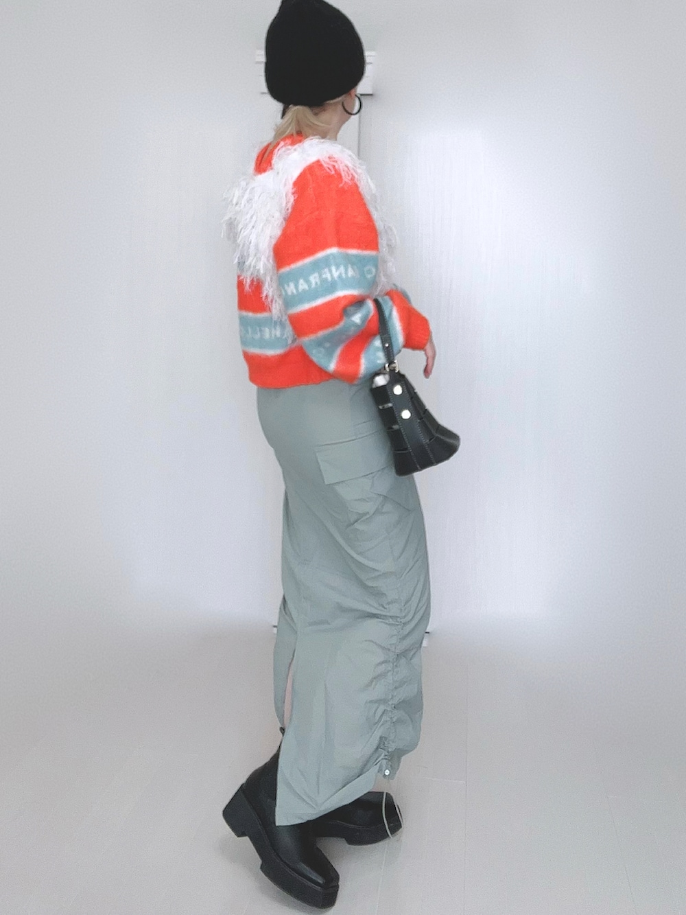 オレンジ系のニット/セーター、ホワイト系のベスト、ブラック系のショルダーバッグを着用したレディースの冬コーディネートの2枚目の写真