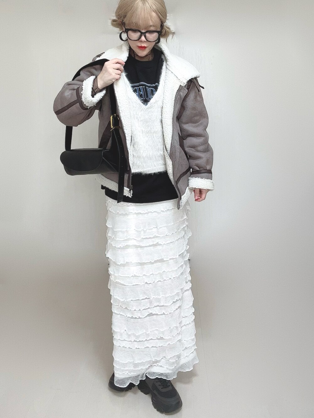 グレー系のムートンコート、ホワイト系のベスト、ブラック系のTシャツ/カットソーを着用したレディースの冬コーディネートの2枚目の写真