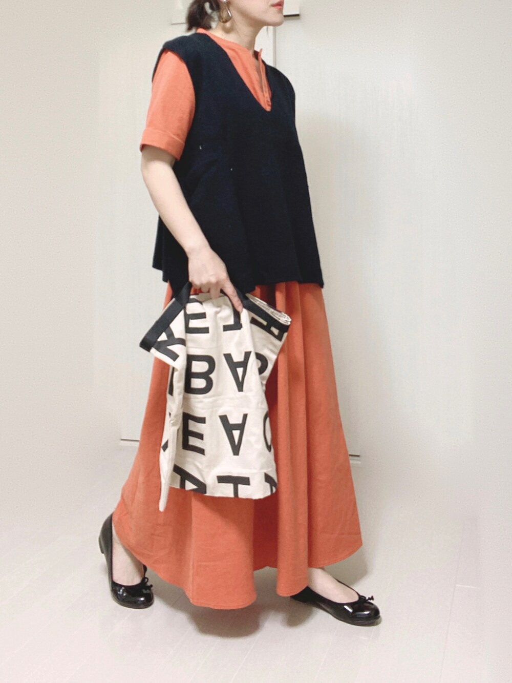 オレンジ系のワンピース、ブラック系のベスト、ホワイト系のトートバッグを着用したレディースの夏コーディネートの4枚目の写真