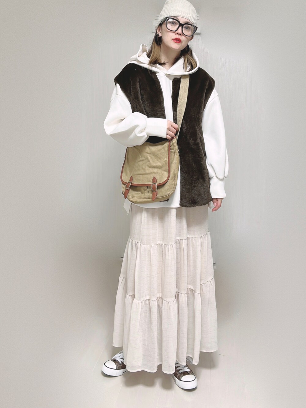 ブラウン系のベスト、ホワイト系のパーカー、ベージュ系のショルダーバッグを着用したレディースの秋コーディネートの2枚目の写真