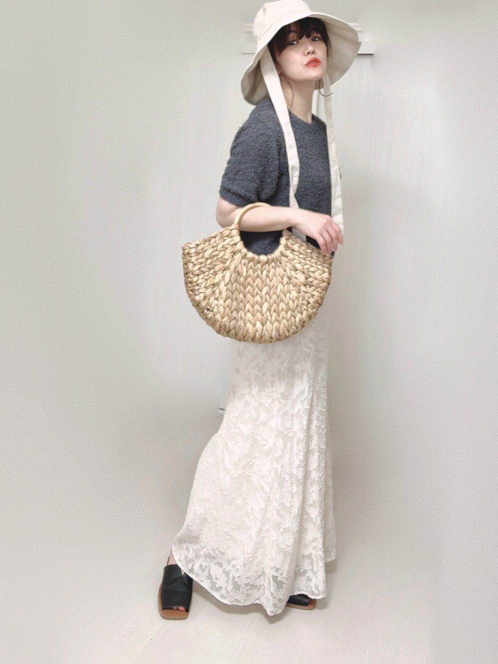 グレー系のニット/セーター、ホワイト系のスカート、ベージュ系のかごバッグを着用したレディースの夏コーディネートの2枚目の写真