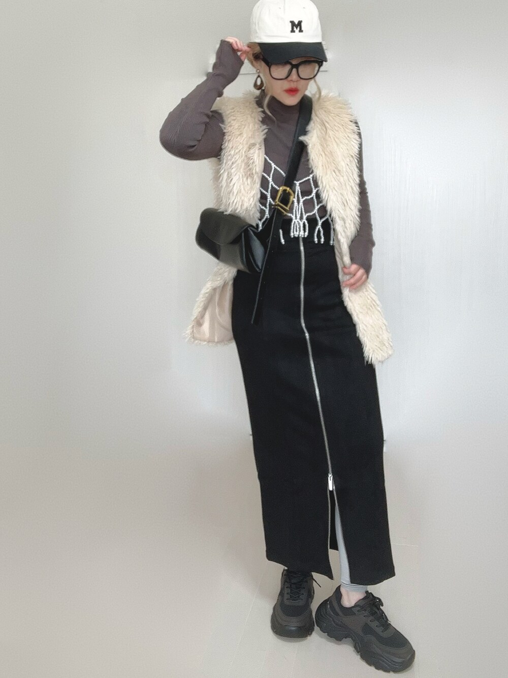 ブラック系のスカート、ホワイト系のベスト、ブラック系のスニーカーを着用したレディースの秋コーディネートの4枚目の写真