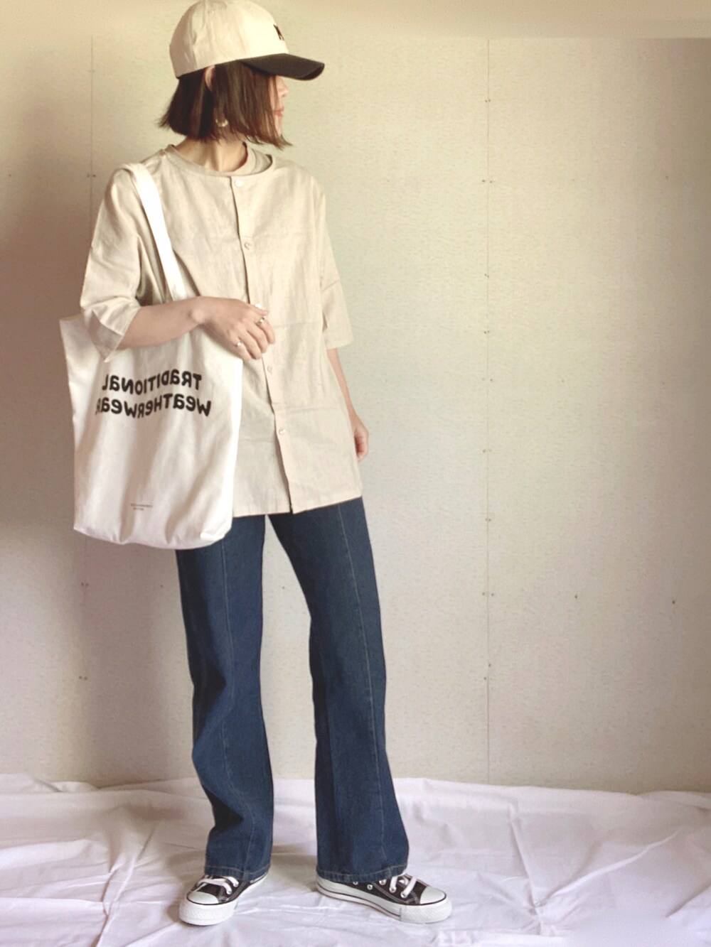 ホワイト系のトートバッグ、ベージュ系のチュニック、ブルー系のデニムパンツを着用したレディースの夏コーディネートの4枚目の写真