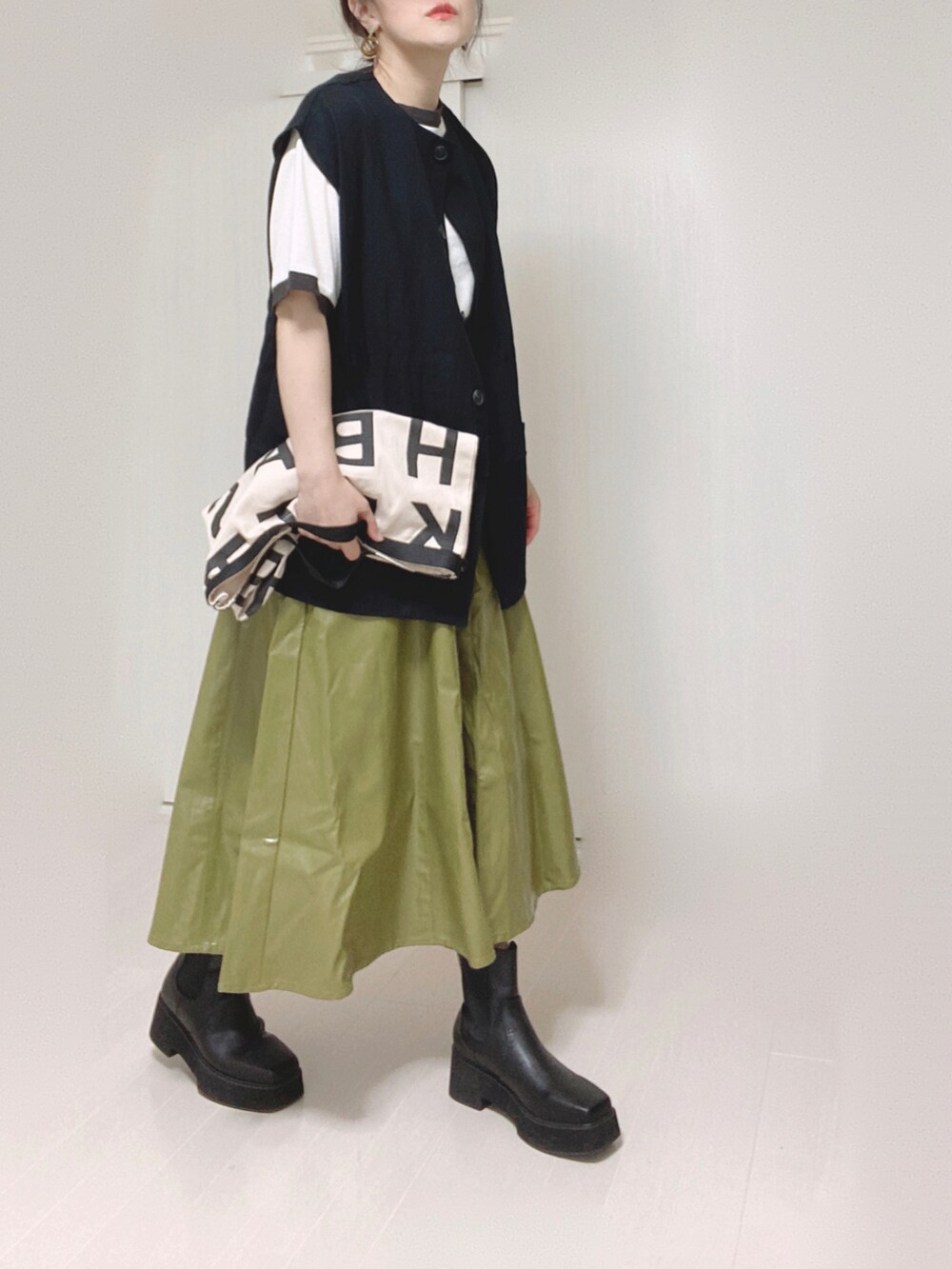 ブラック系のベスト、ホワイト系のトートバッグ、グリーン系のスカートを着用したレディースの秋コーディネートの3枚目の写真