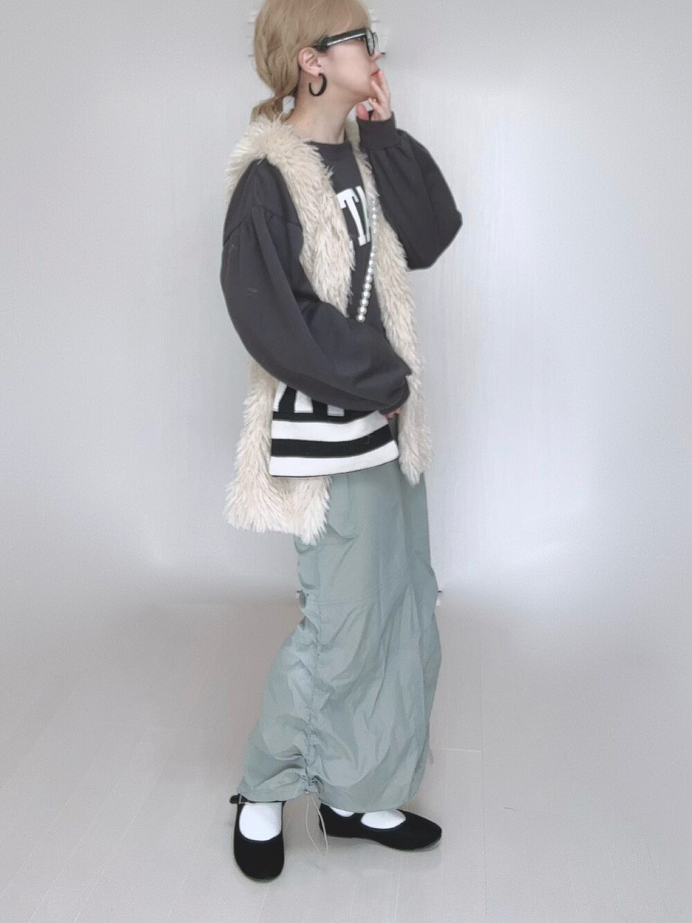 グリーン系のスカート、ホワイト系のベスト、ホワイト系のショルダーバッグを着用したレディースの冬コーディネートの2枚目の写真