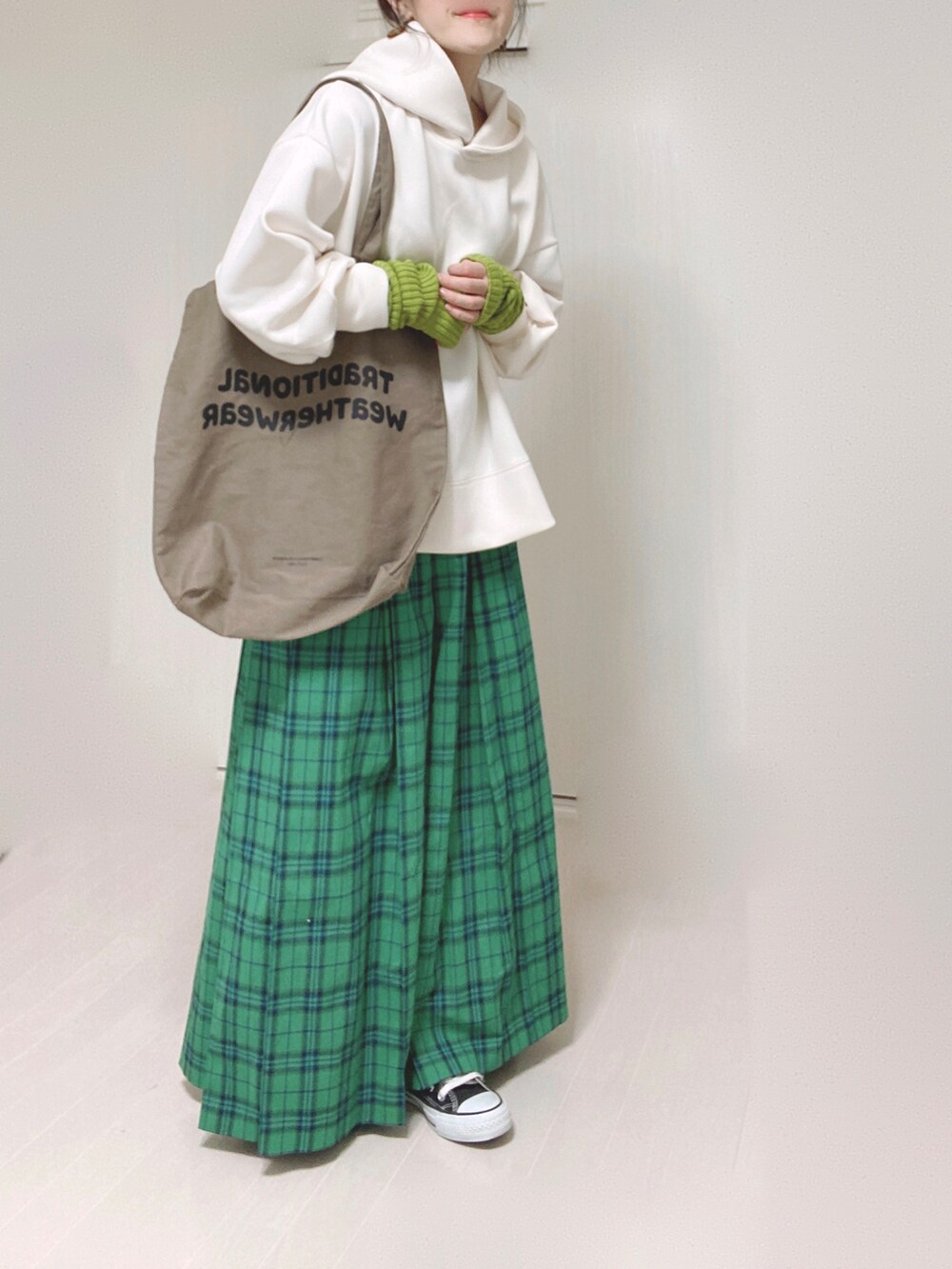 ホワイト系のパーカー、ブラウン系のトートバッグ、グリーン系のスカートを着用したレディースの秋コーディネートの4枚目の写真