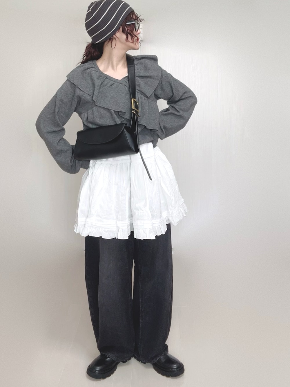 グレー系のニット/セーター、ブラック系のデニムパンツ、ホワイト系のスカートを着用したレディースの秋コーディネートの3枚目の写真