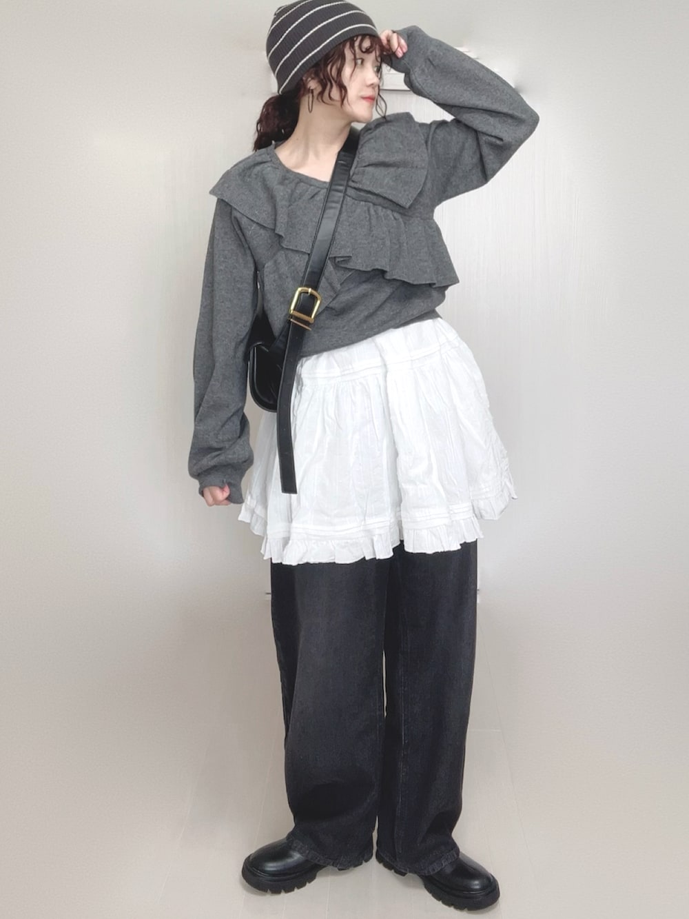 グレー系のニット/セーター、ブラック系のデニムパンツ、ホワイト系のスカートを着用したレディースの秋コーディネートの2枚目の写真