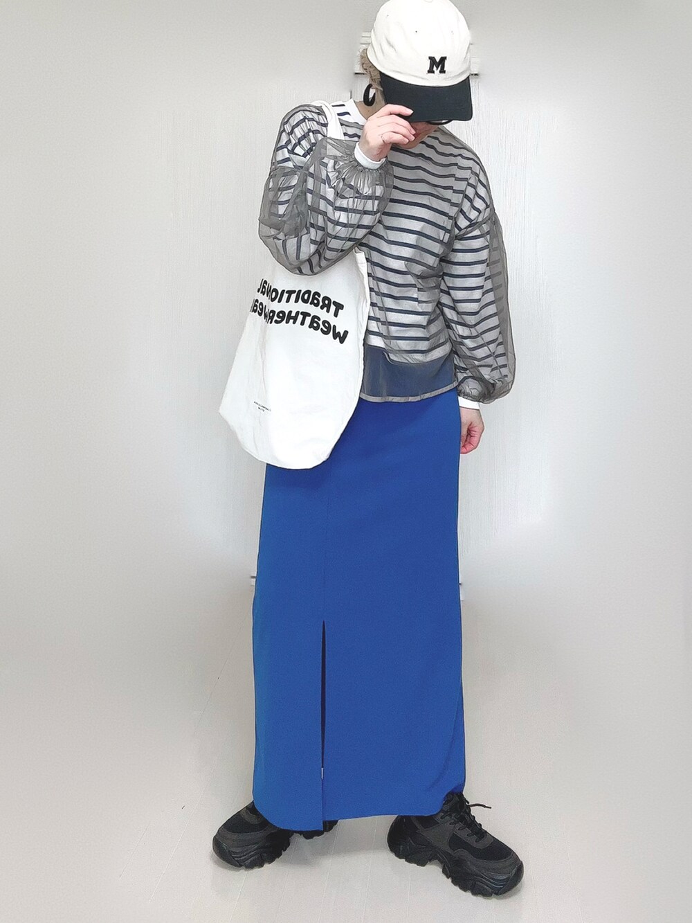 ブルー系のスカート、ホワイト系のトートバッグ、ブラック系のスニーカーを着用したレディースの春コーディネートの3枚目の写真