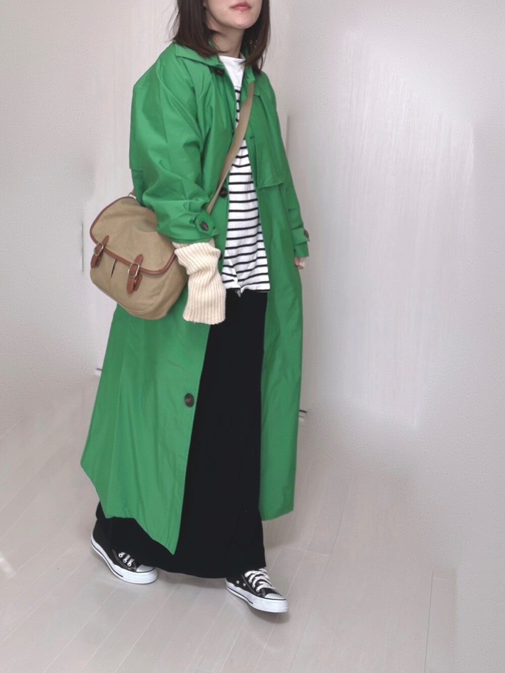 グリーン系のトレンチコート、ブラック系のTシャツ/カットソー、ベージュ系のショルダーバッグを着用したレディースの冬コーディネートの2枚目の写真