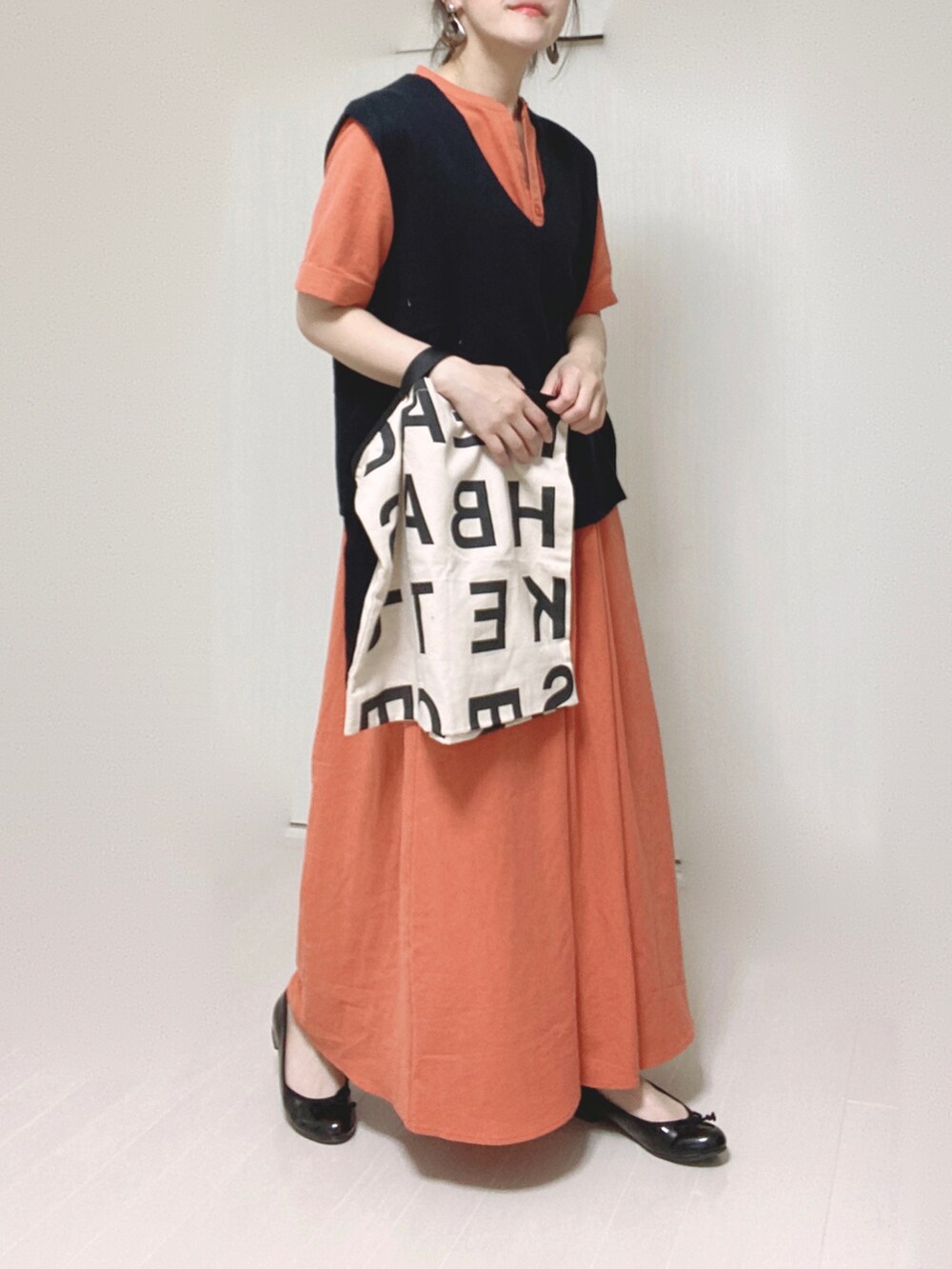 オレンジ系のワンピース、ブラック系のベスト、ホワイト系のトートバッグを着用したレディースの夏コーディネートの5枚目の写真