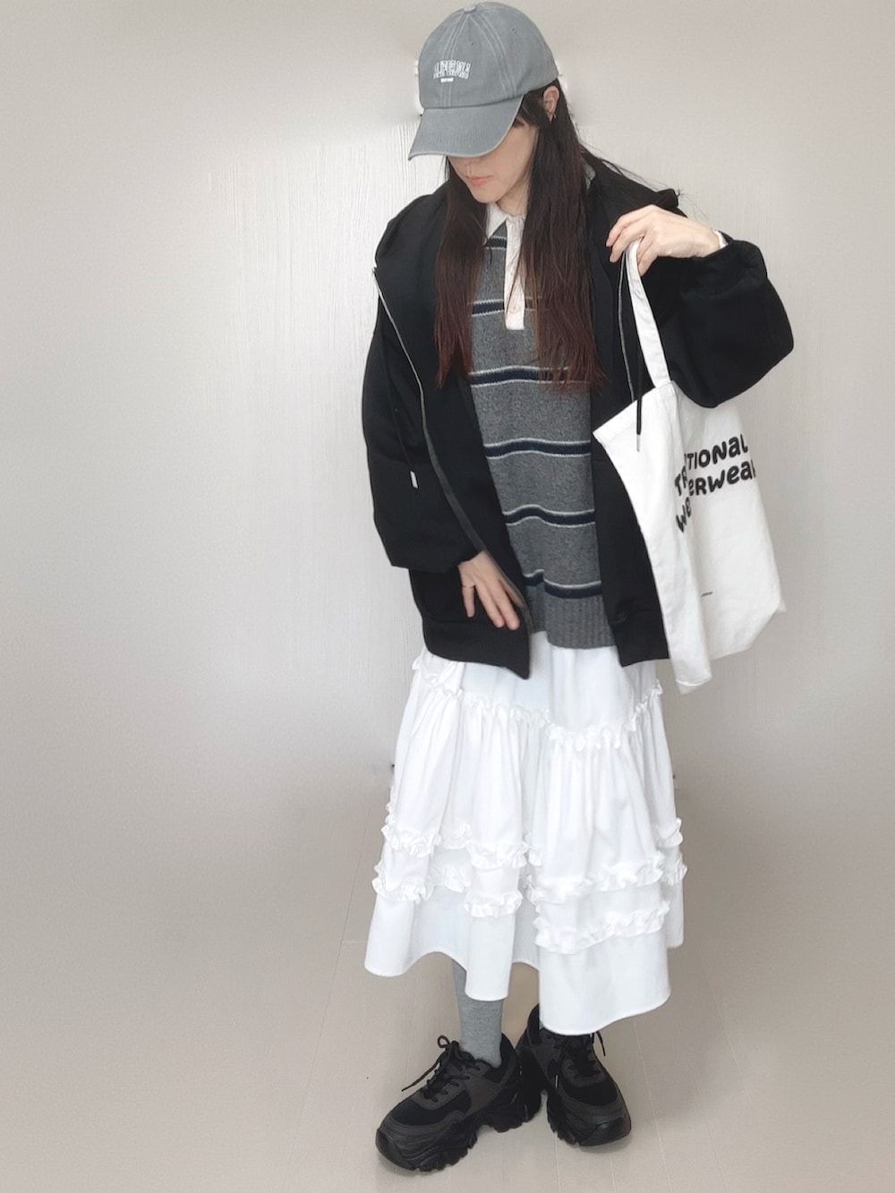 ブラック系のパーカー、グレー系のニット/セーター、ホワイト系のスカートを着用したレディースの春コーディネートの2枚目の写真