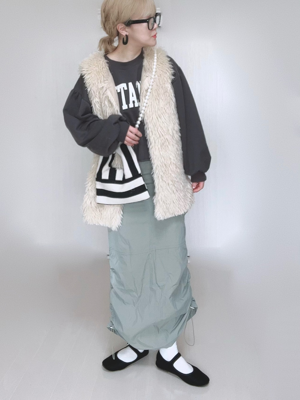 グリーン系のスカート、ホワイト系のベスト、ホワイト系のショルダーバッグを着用したレディースの冬コーディネートの4枚目の写真