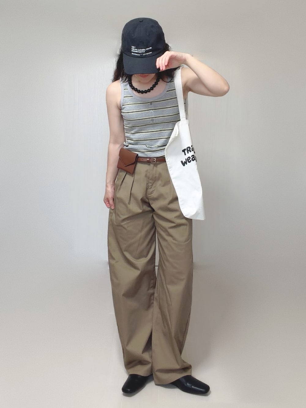 グレー系のタンクトップ、ブラック系のスリッポン、ベージュ系のチノパンツを着用したレディースの夏コーディネートの2枚目の写真