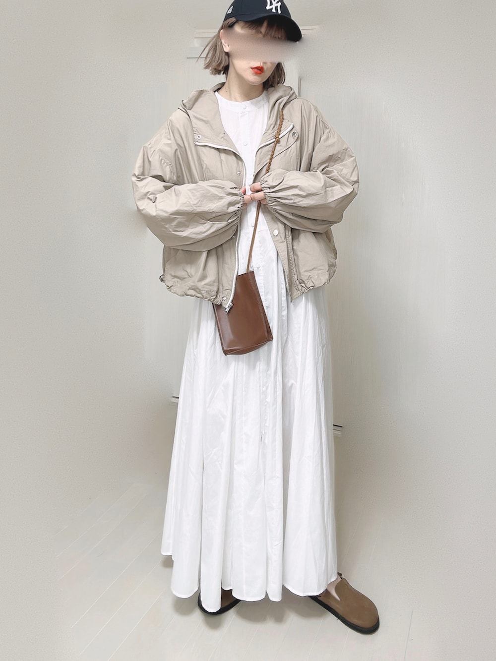 ベージュ系のマウンテンパーカー、ホワイト系のシャツワンピース、ブラウン系のショルダーバッグを着用したレディースの春コーディネートの4枚目の写真