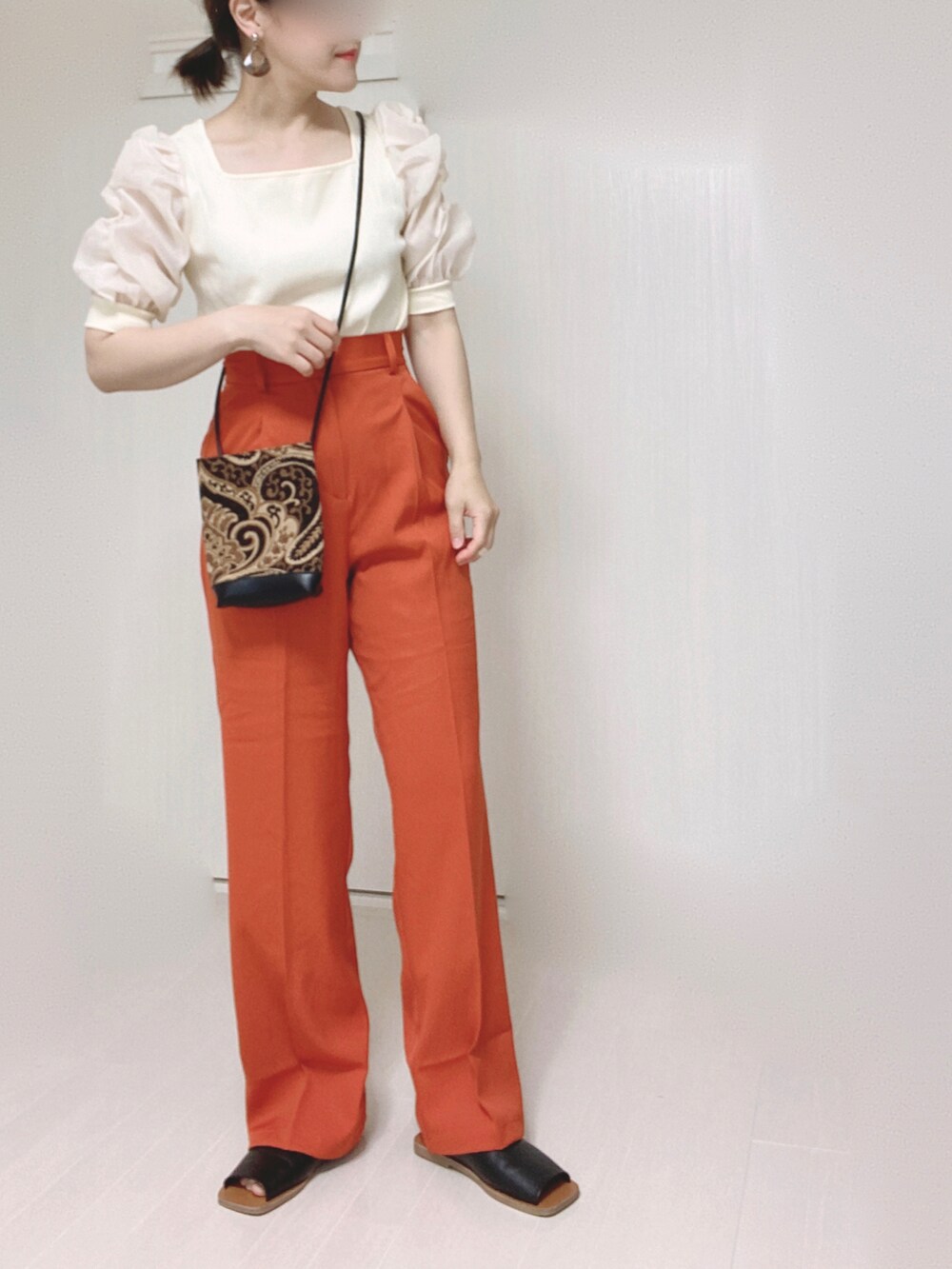 オレンジ系のスラックス、ホワイト系のTシャツ/カットソー、ブラック系のショルダーバッグを着用したレディースの夏コーディネートの4枚目の写真