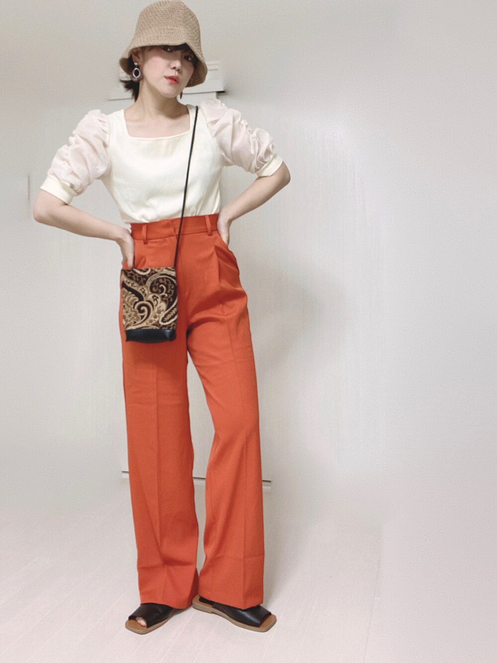 オレンジ系のスラックス、ホワイト系のTシャツ/カットソー、ブラック系のショルダーバッグを着用したレディースの夏コーディネートの3枚目の写真