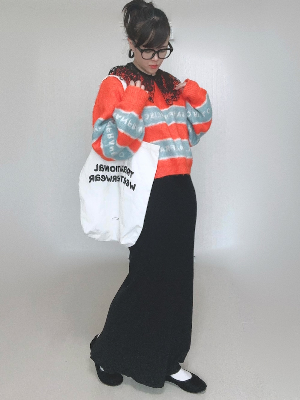 オレンジ系のニット/セーター、ホワイト系のトートバッグ、ブラック系のスカートを着用したレディースの冬コーディネートの5枚目の写真