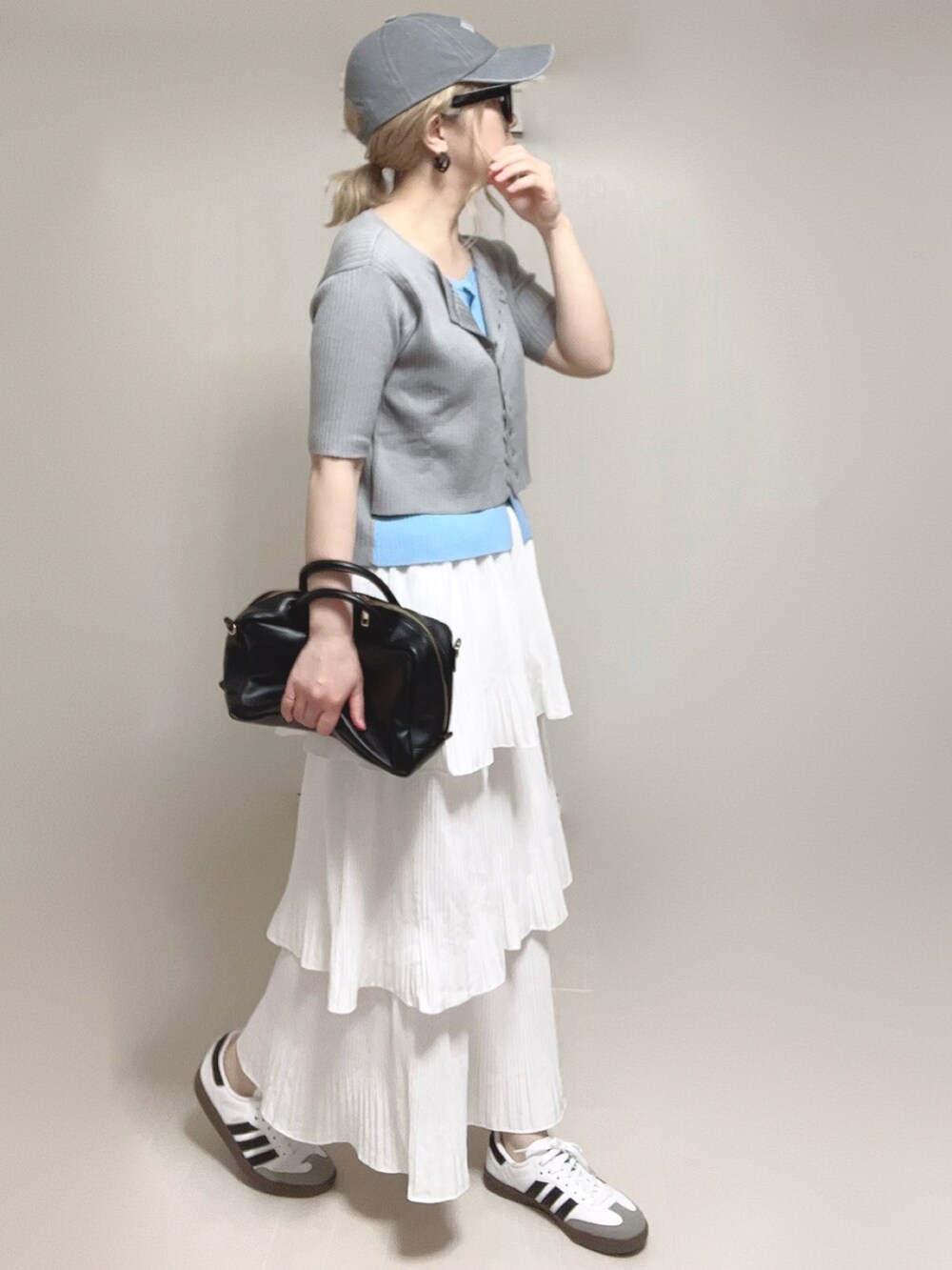 グレー系のニット/セーター、ブラック系のボストンバッグ、ホワイト系のスカートを着用したレディースの夏コーディネートの2枚目の写真