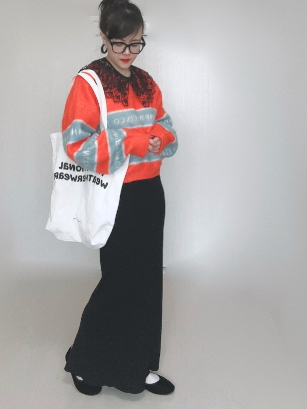 オレンジ系のニット/セーター、ホワイト系のトートバッグ、ブラック系のスカートを着用したレディースの冬コーディネートの4枚目の写真