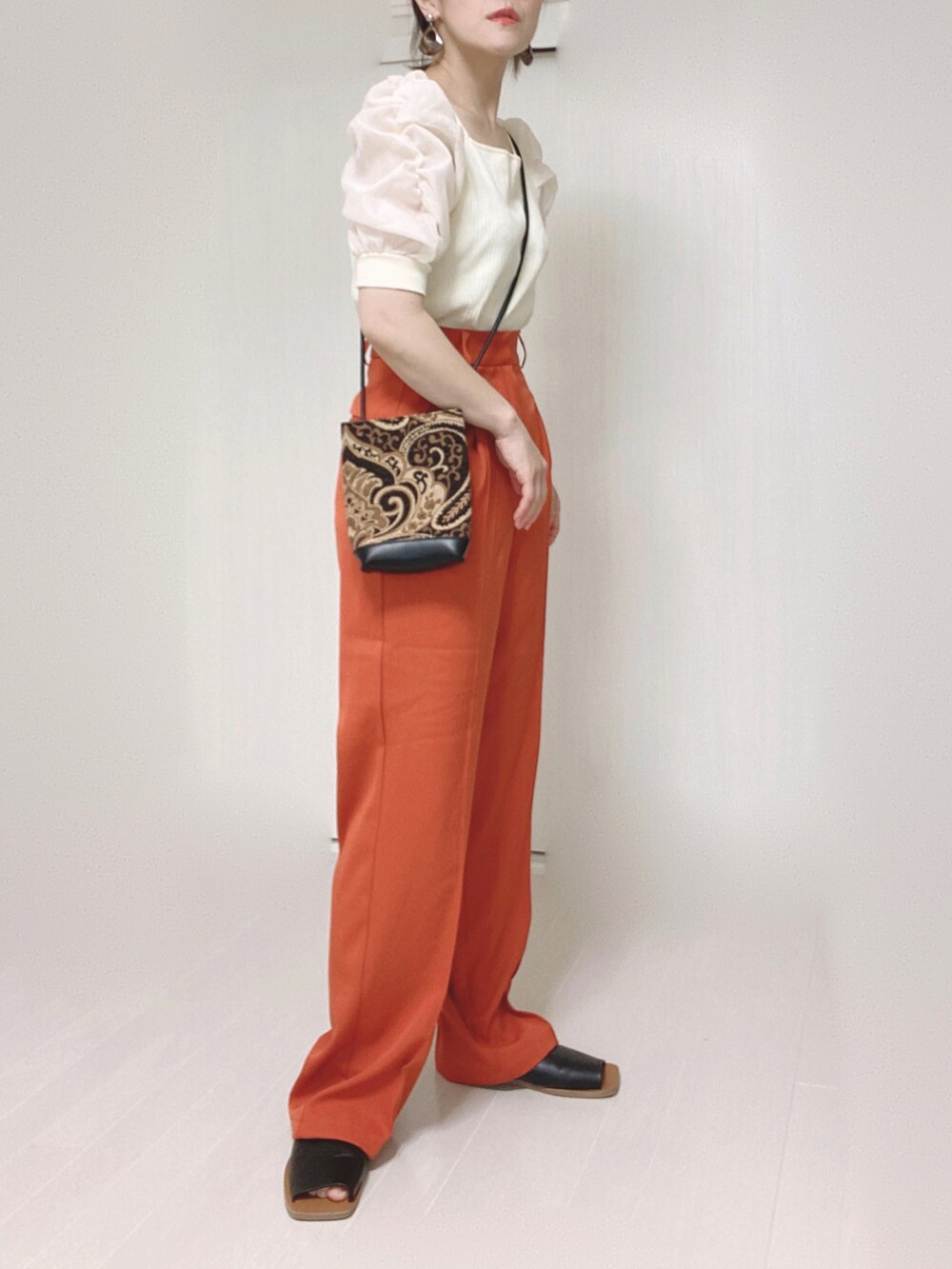 オレンジ系のスラックス、ホワイト系のTシャツ/カットソー、ブラック系のショルダーバッグを着用したレディースの夏コーディネートの2枚目の写真