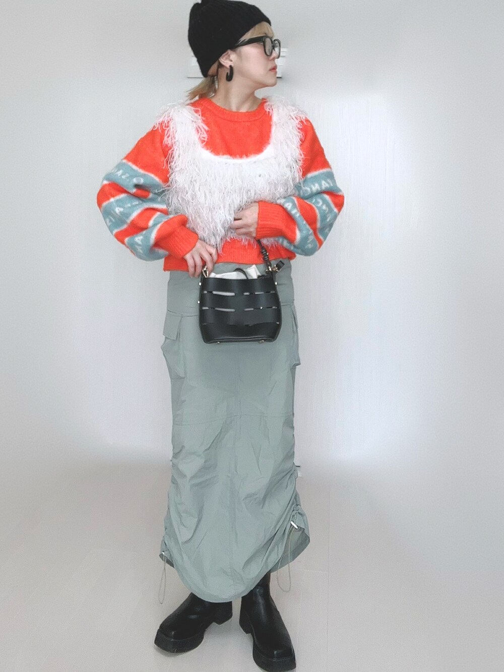 オレンジ系のニット/セーター、ホワイト系のベスト、ブラック系のショルダーバッグを着用したレディースの冬コーディネートの3枚目の写真