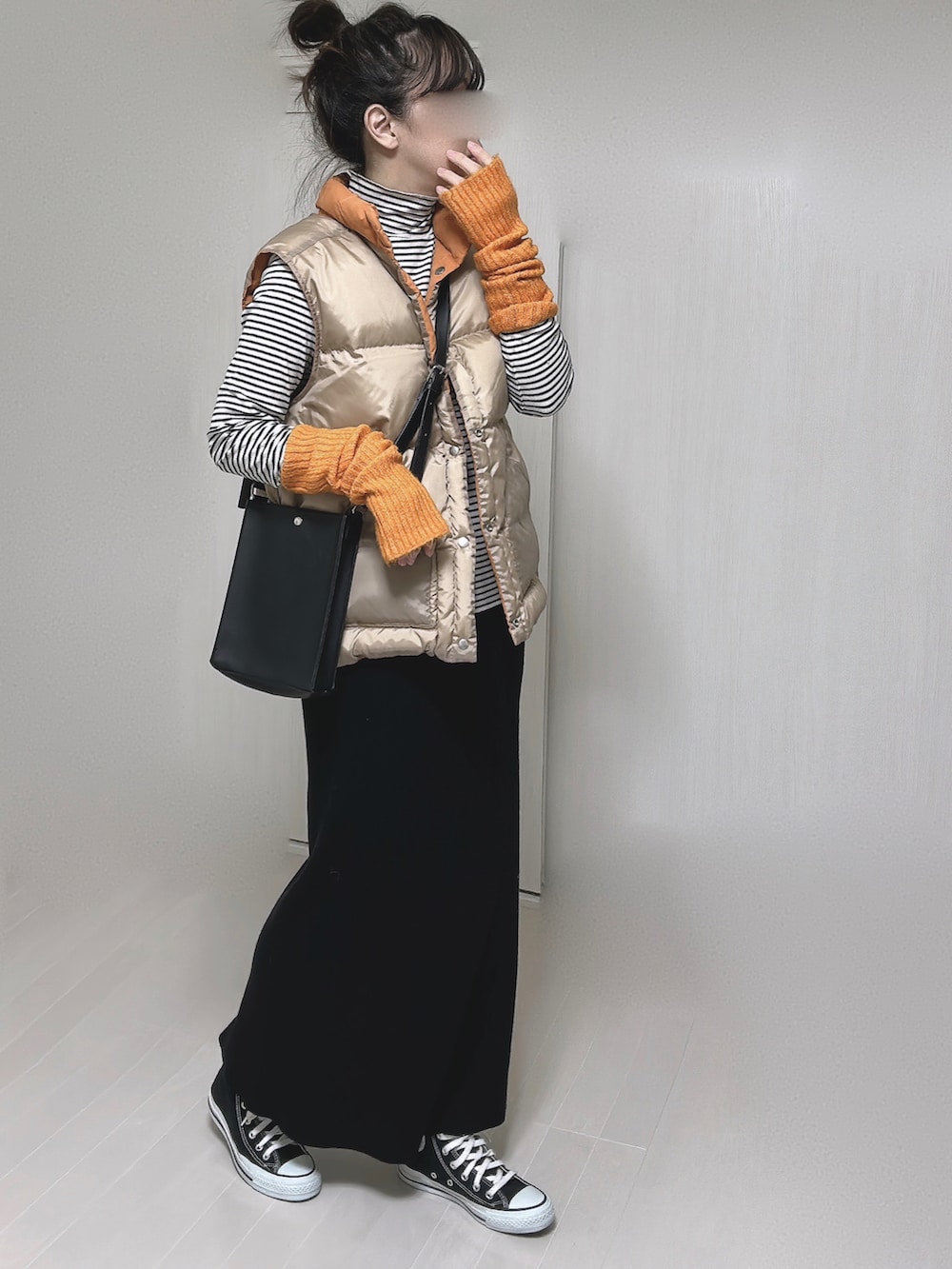オレンジ系のダウンベスト、ブラック系のショルダーバッグ、ブラック系のスカートを着用したレディースの冬コーディネートの5枚目の写真