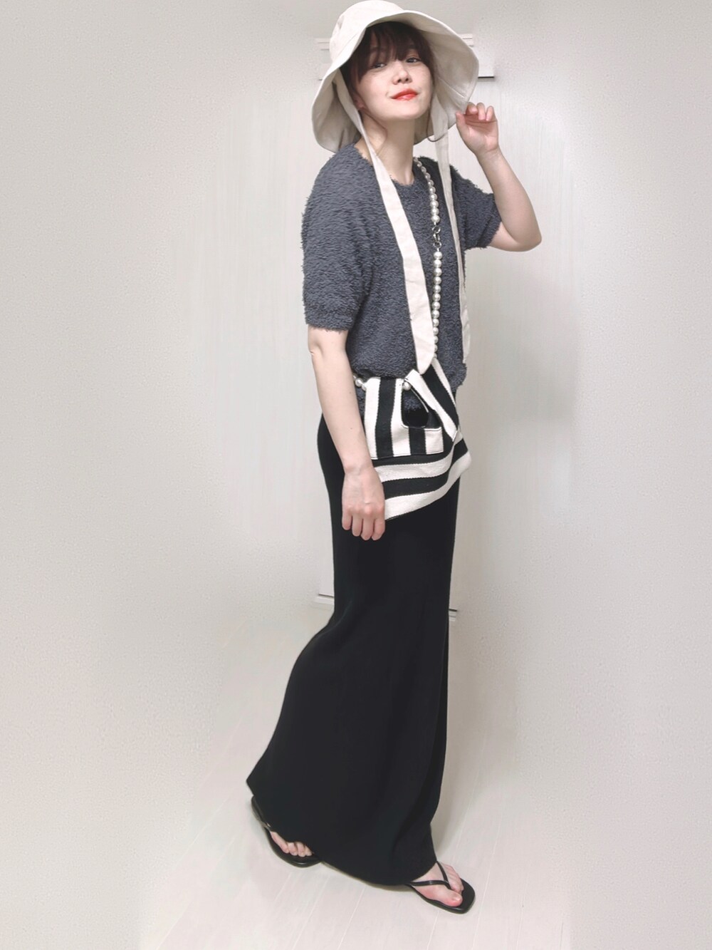 グレー系のニット/セーター、ホワイト系のショルダーバッグ、ブラック系のスカートを着用したレディースの夏コーディネートの3枚目の写真
