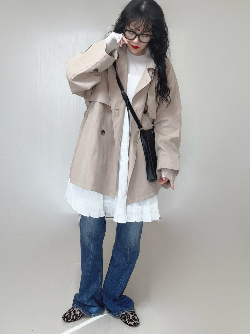 ベージュ系のトレンチコート、ホワイト系のワンピース、ブラック系のショルダーバッグを着用したレディースの春コーディネートの2枚目の写真
