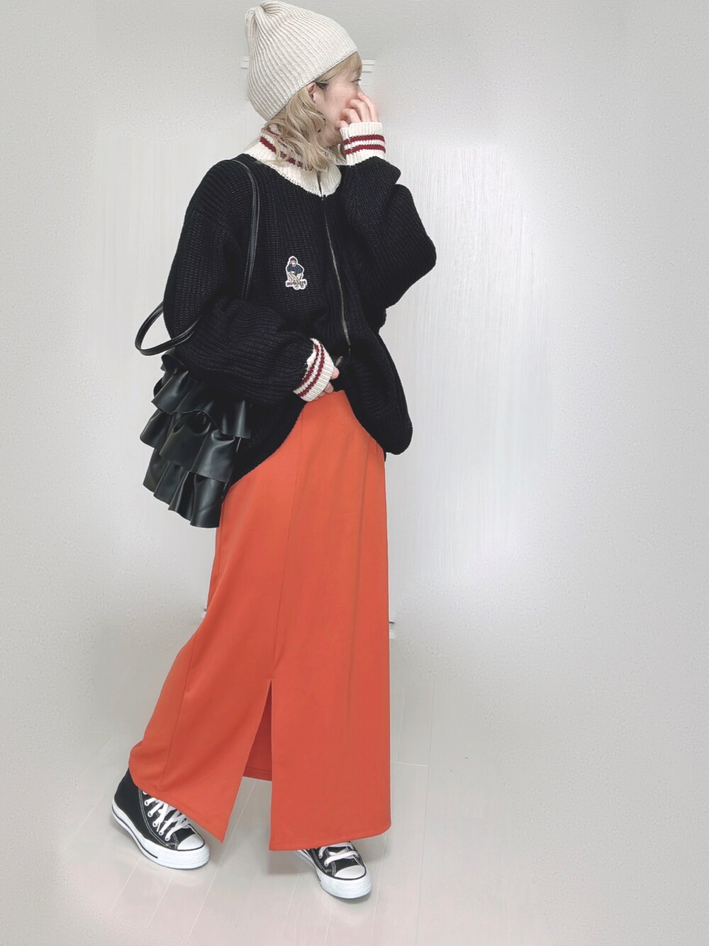 ブラック系のニット/セーター、オレンジ系のスカート、ブラック系のスニーカーを着用したレディースの秋コーディネートの2枚目の写真