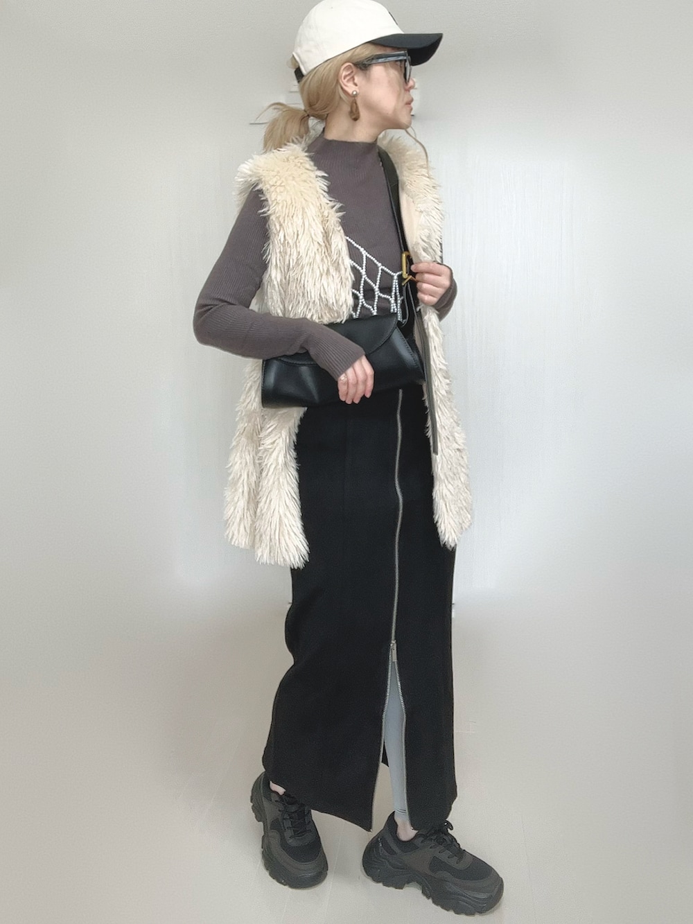 ブラック系のスカート、ホワイト系のベスト、ブラック系のスニーカーを着用したレディースの秋コーディネートの5枚目の写真