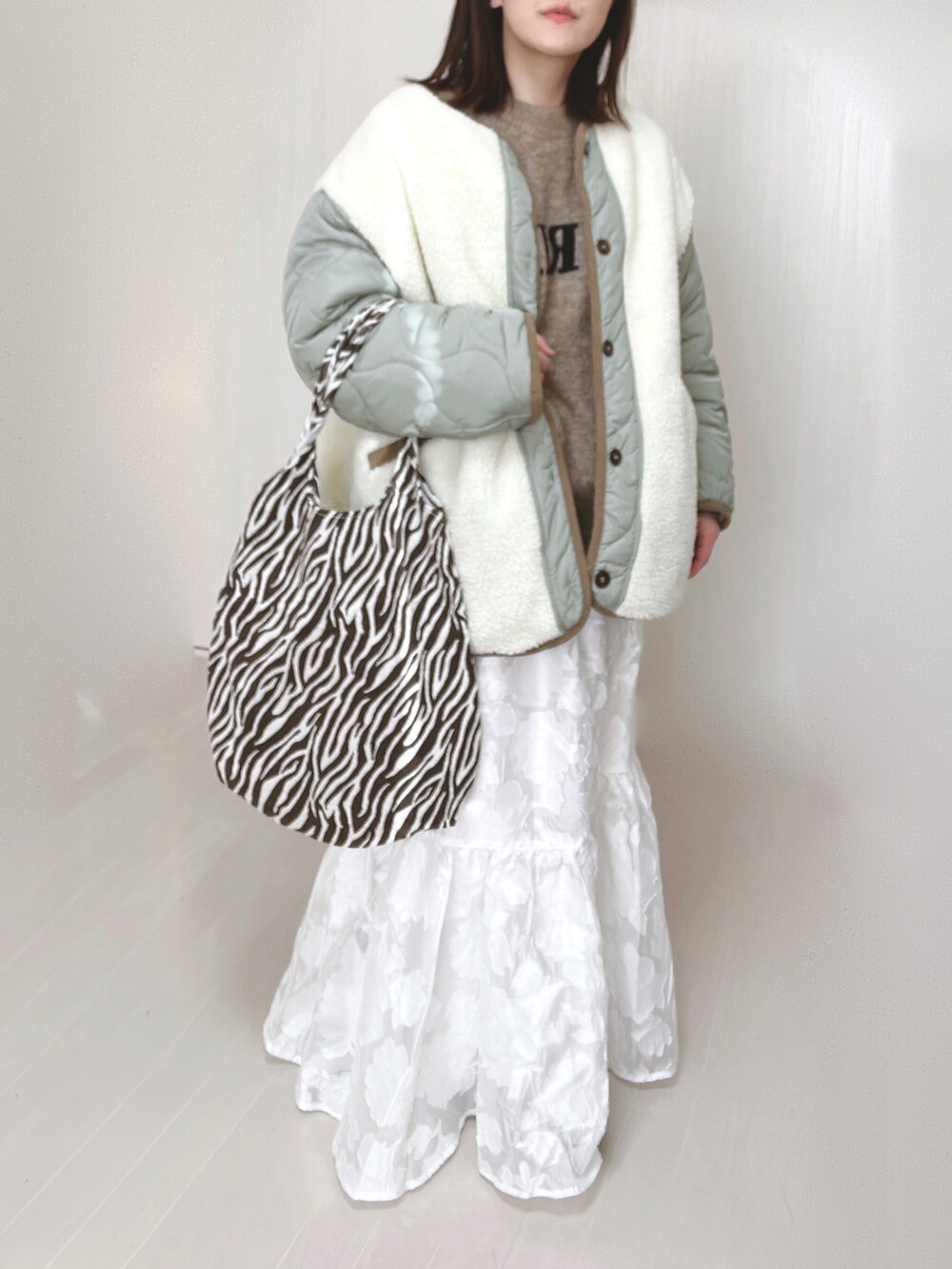 ホワイト系のノーカラージャケット、ベージュ系のニット/セーター、ホワイト系のスカートを着用したレディースの冬コーディネートの4枚目の写真