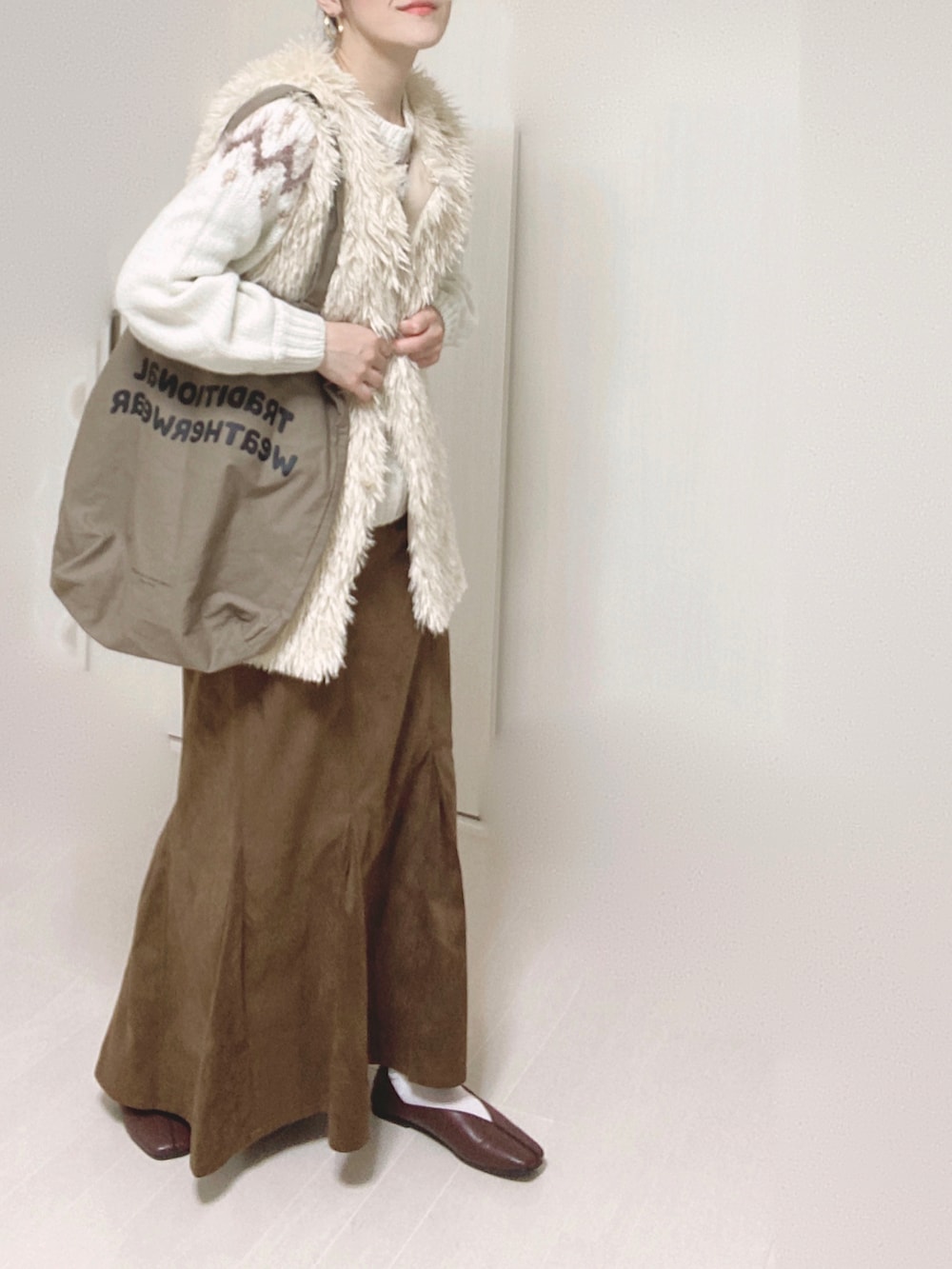 ホワイト系のベスト、ホワイト系のニット/セーター、ブラウン系のスカートを着用したレディースの秋コーディネートの2枚目の写真