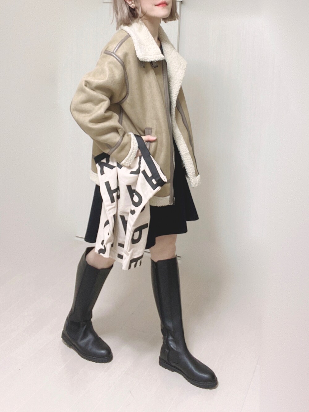 ブラック系のブーツ、ベージュ系のムートンコート、ホワイト系のトートバッグを着用したレディースの秋コーディネートの4枚目の写真