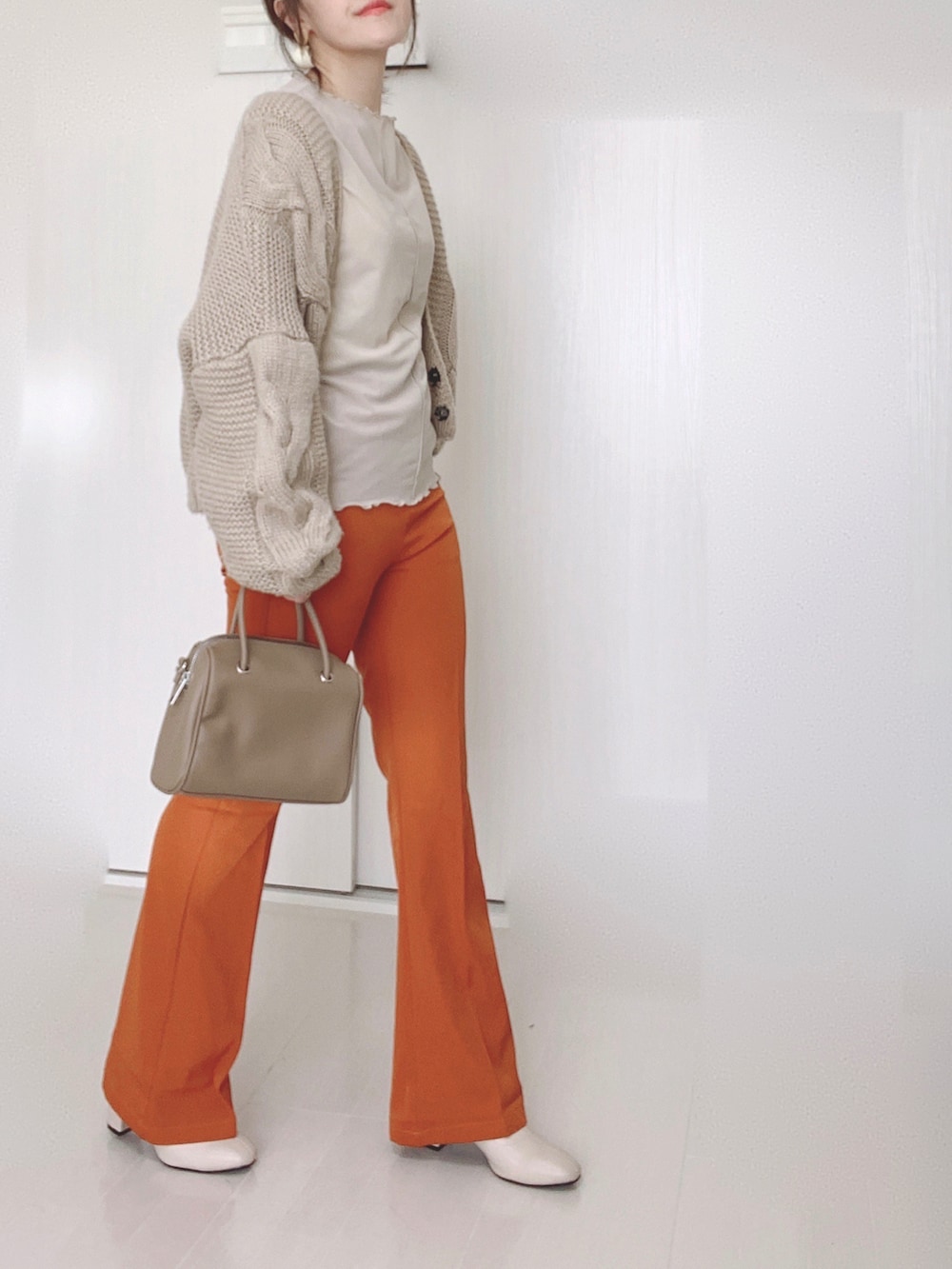 オレンジ系のスラックス、ベージュ系のTシャツ/カットソー、ベージュ系のブーツを着用したレディースの秋コーディネートの3枚目の写真