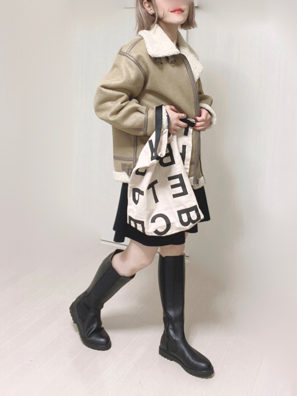 ブラック系のブーツ、ベージュ系のムートンコート、ホワイト系のトートバッグを着用したレディースの秋コーディネートの2枚目の写真