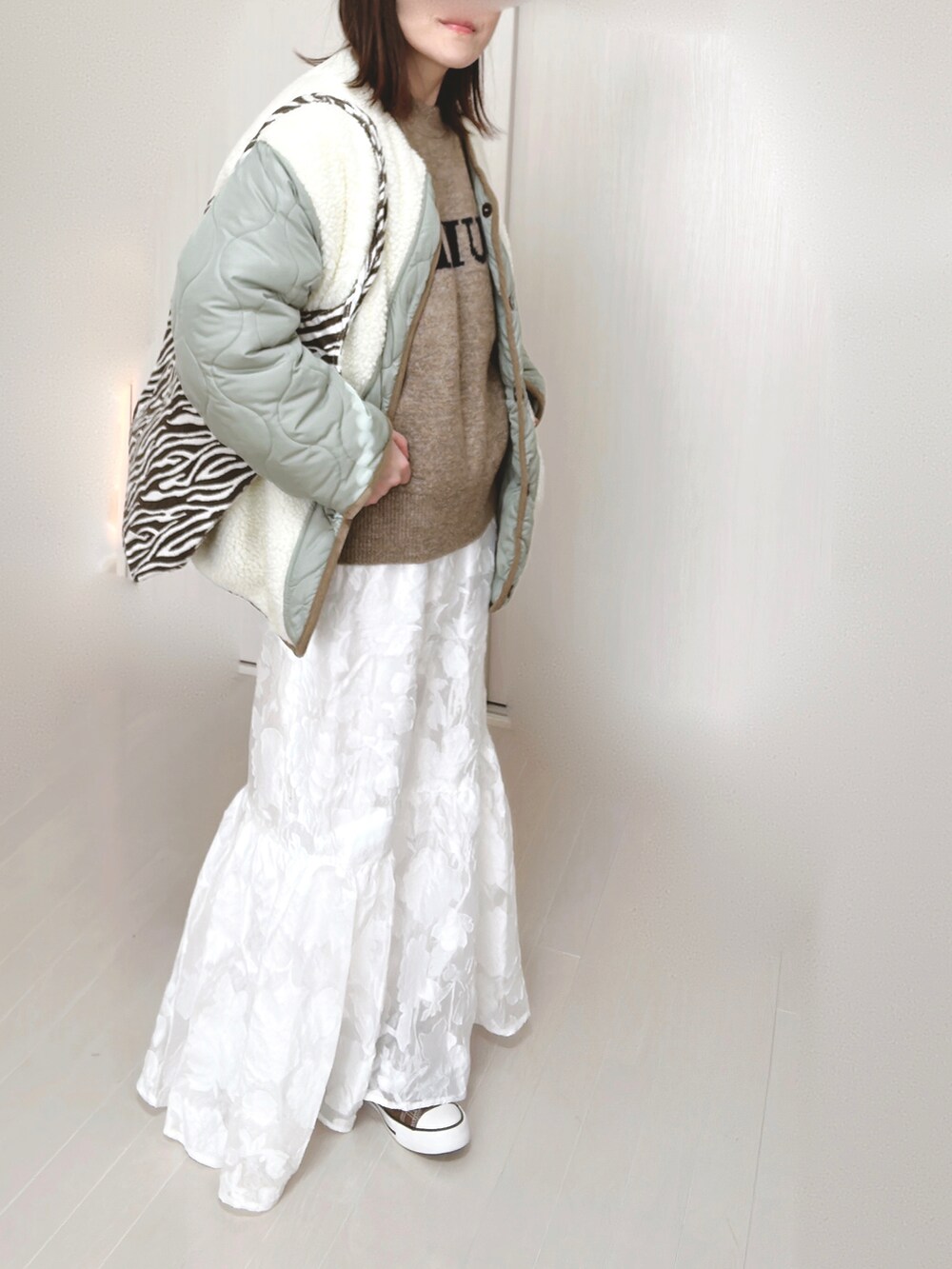 ホワイト系のノーカラージャケット、ベージュ系のニット/セーター、ホワイト系のスカートを着用したレディースの冬コーディネートの2枚目の写真