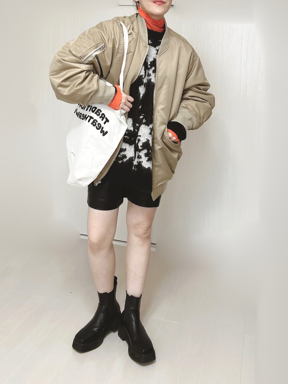 ベージュ系のMA-1、ホワイト系のトートバッグ、ブラック系のニット/セーターを着用したレディースの冬コーディネートの3枚目の写真