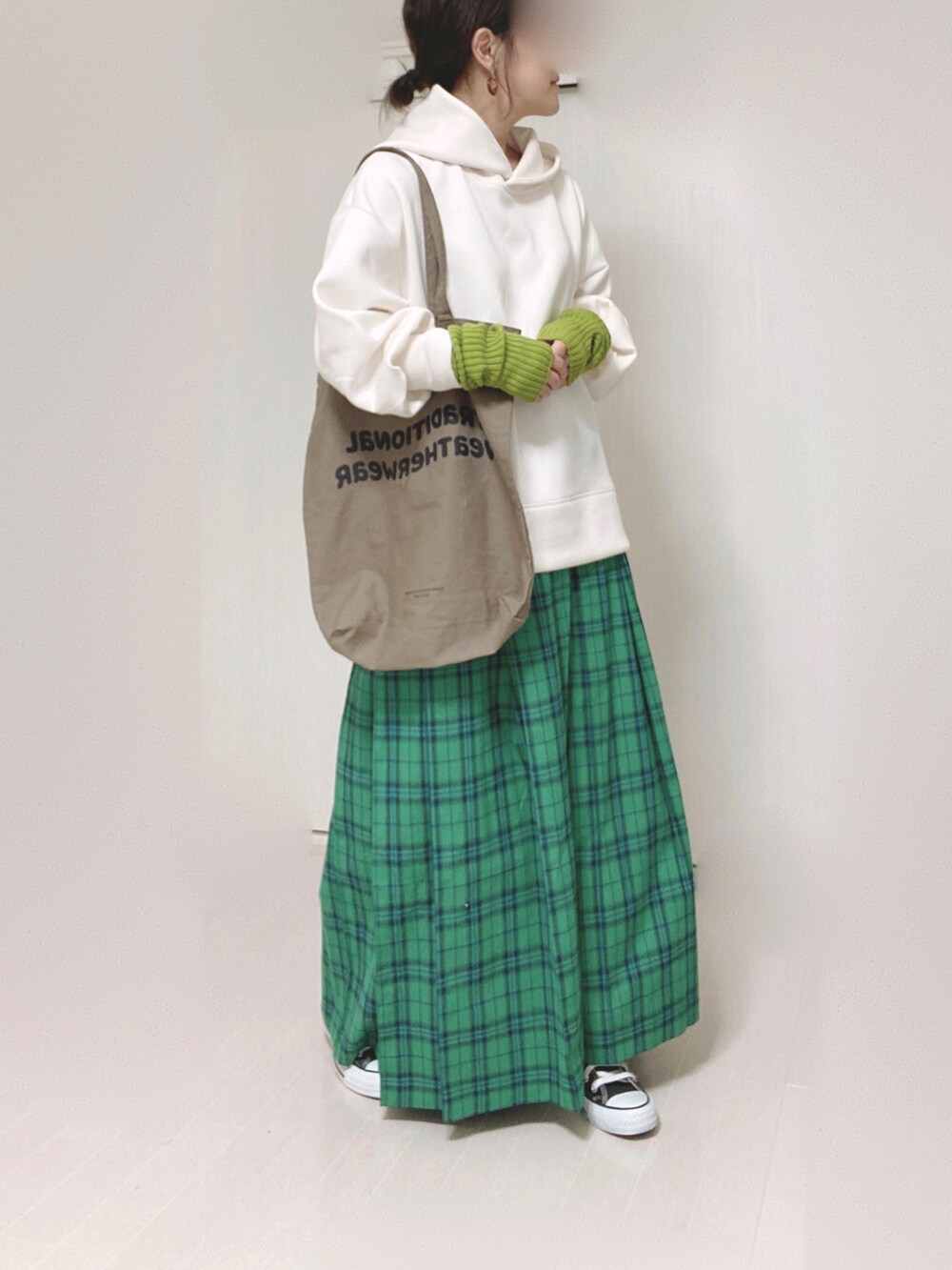 ホワイト系のパーカー、ブラウン系のトートバッグ、グリーン系のスカートを着用したレディースの秋コーディネートの3枚目の写真