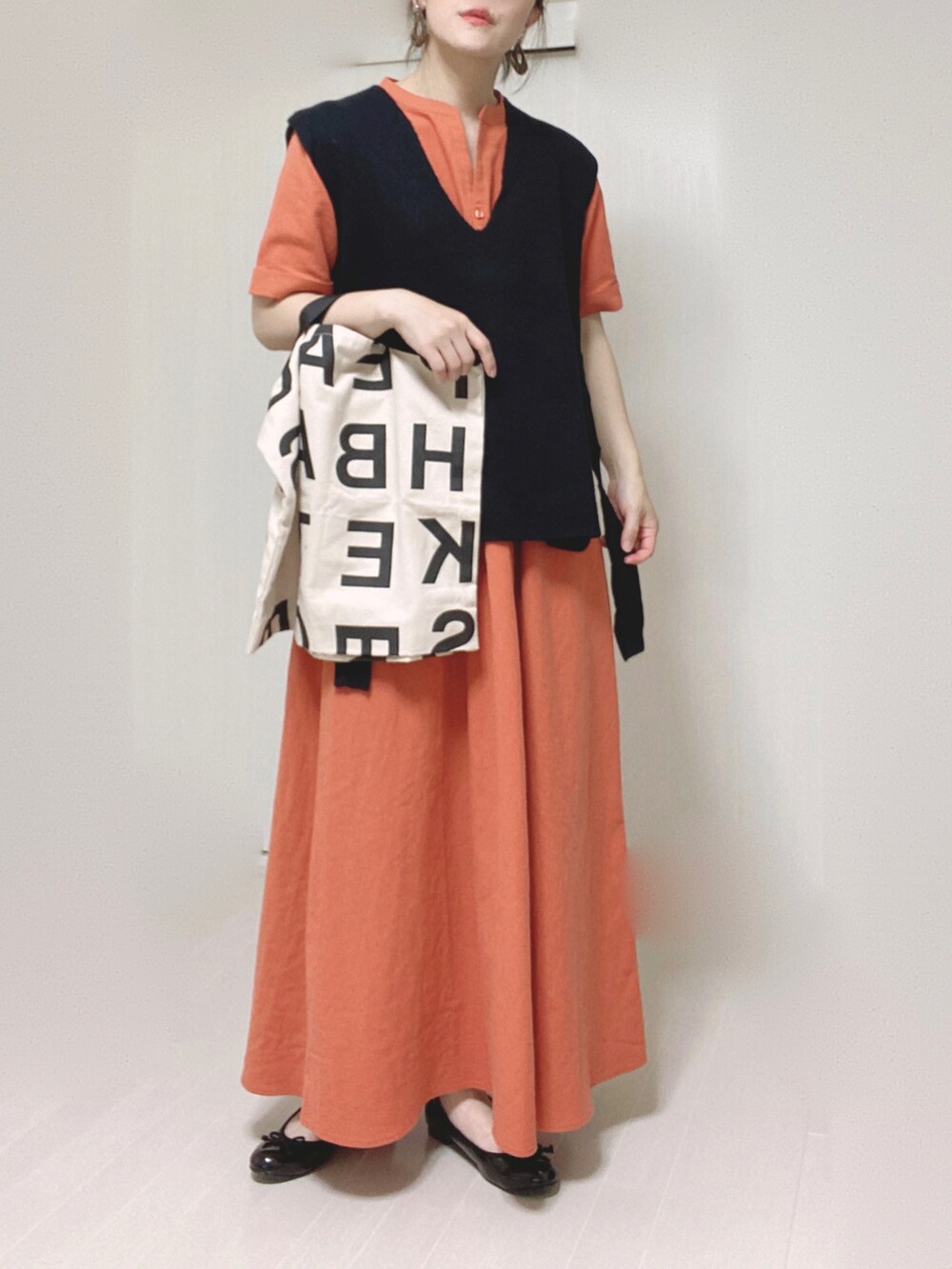 オレンジ系のワンピース、ブラック系のベスト、ホワイト系のトートバッグを着用したレディースの夏コーディネートの3枚目の写真