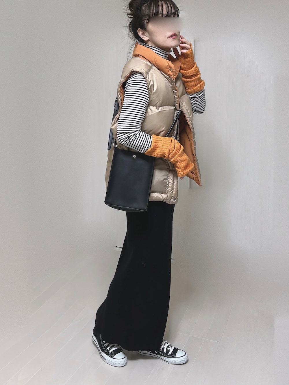 オレンジ系のダウンベスト、ブラック系のショルダーバッグ、ブラック系のスカートを着用したレディースの冬コーディネートの4枚目の写真